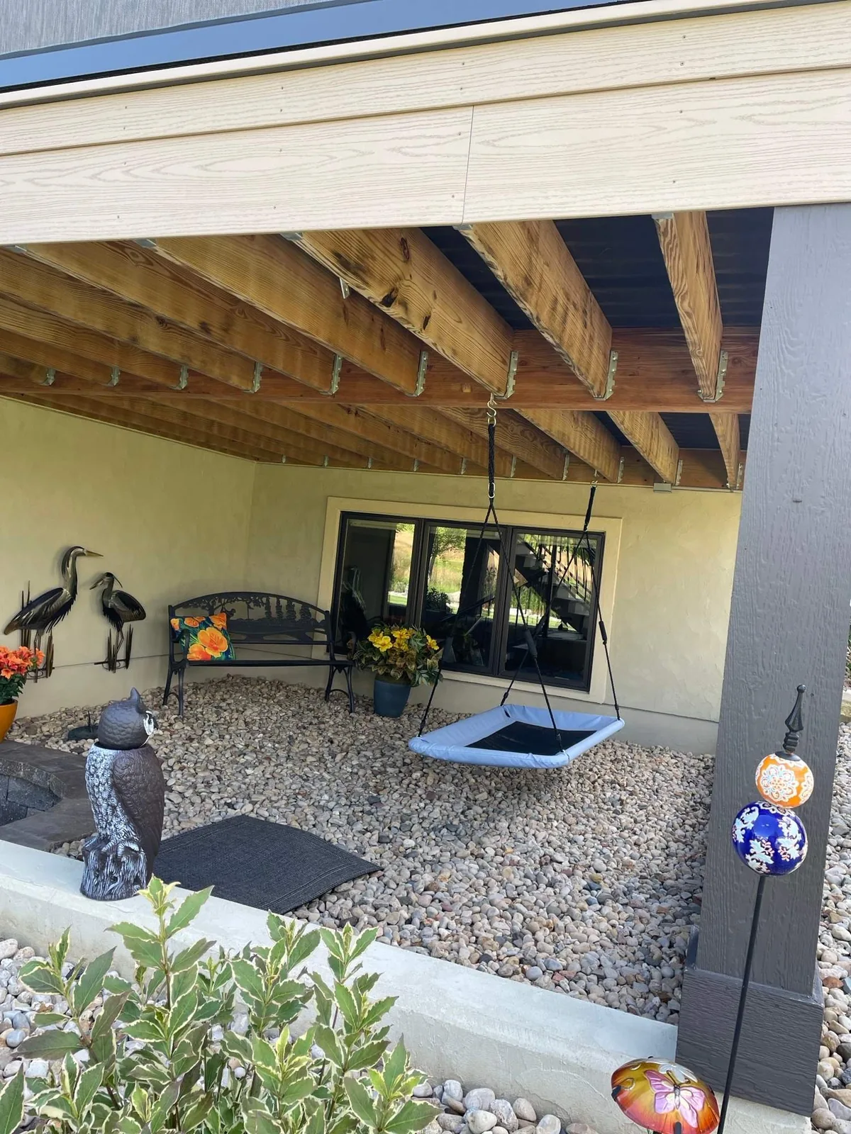 Exposed wood deck joists and a beam above a gravel patio with a hanging swing