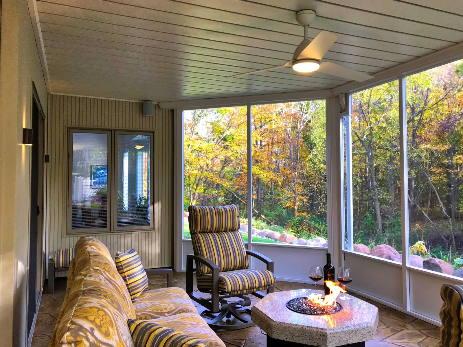 Screened outdoor room with an Under Deck Oasis ceiling, ceiling fan, and fire table